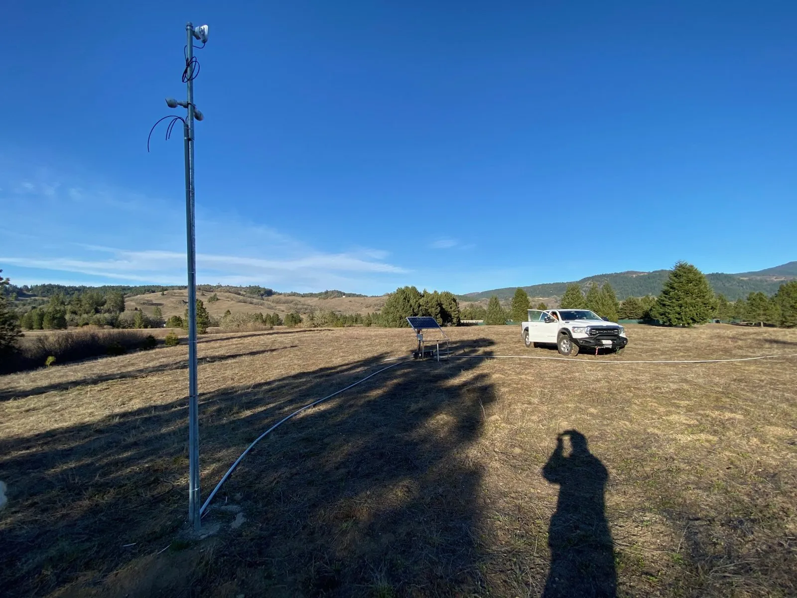 Solar-powered camera pole standing in a dry field with a pickup truck in the distance